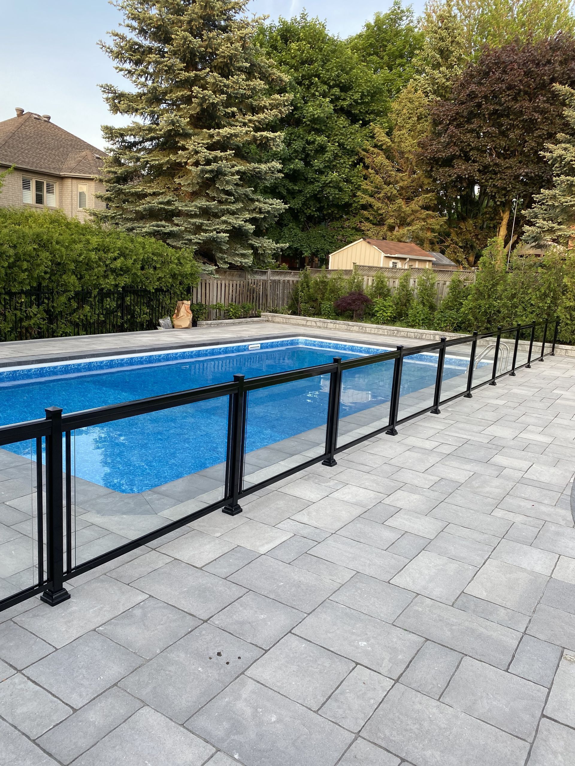 A swimming pool surrounded by a glass fence in a backyard.