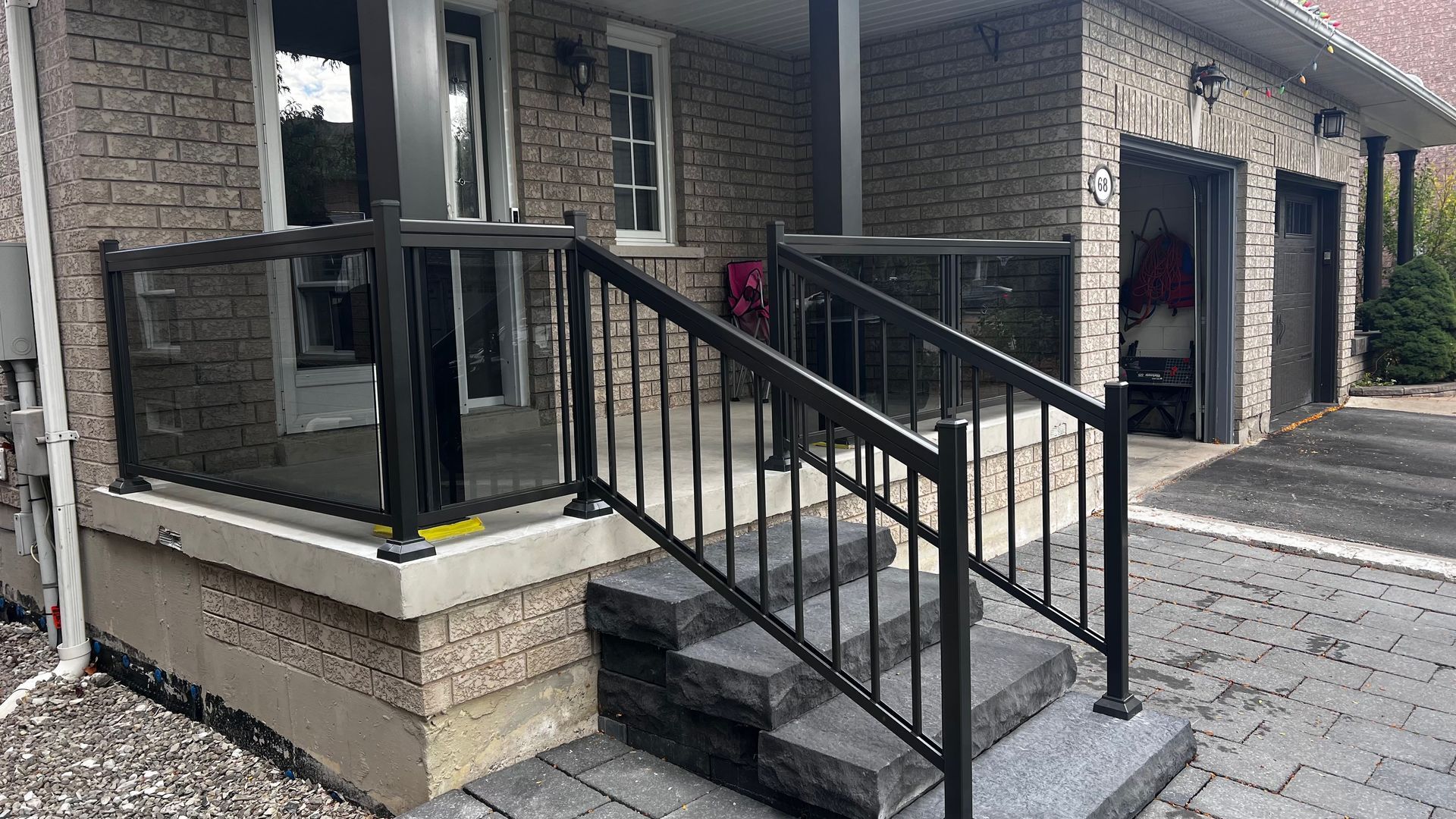 Black railing and glass panel front porch with stone steps leading up to the house.