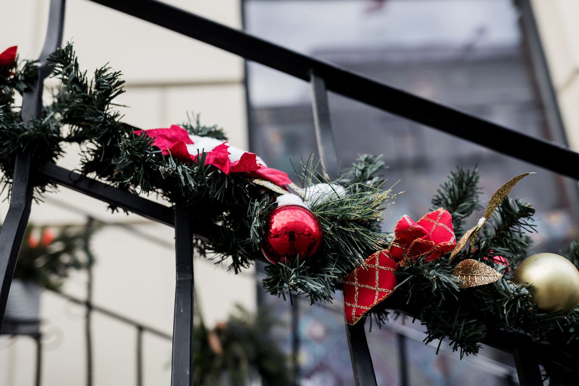 Christmas garland with red bows, ornaments, and gold accents on a black railing.
