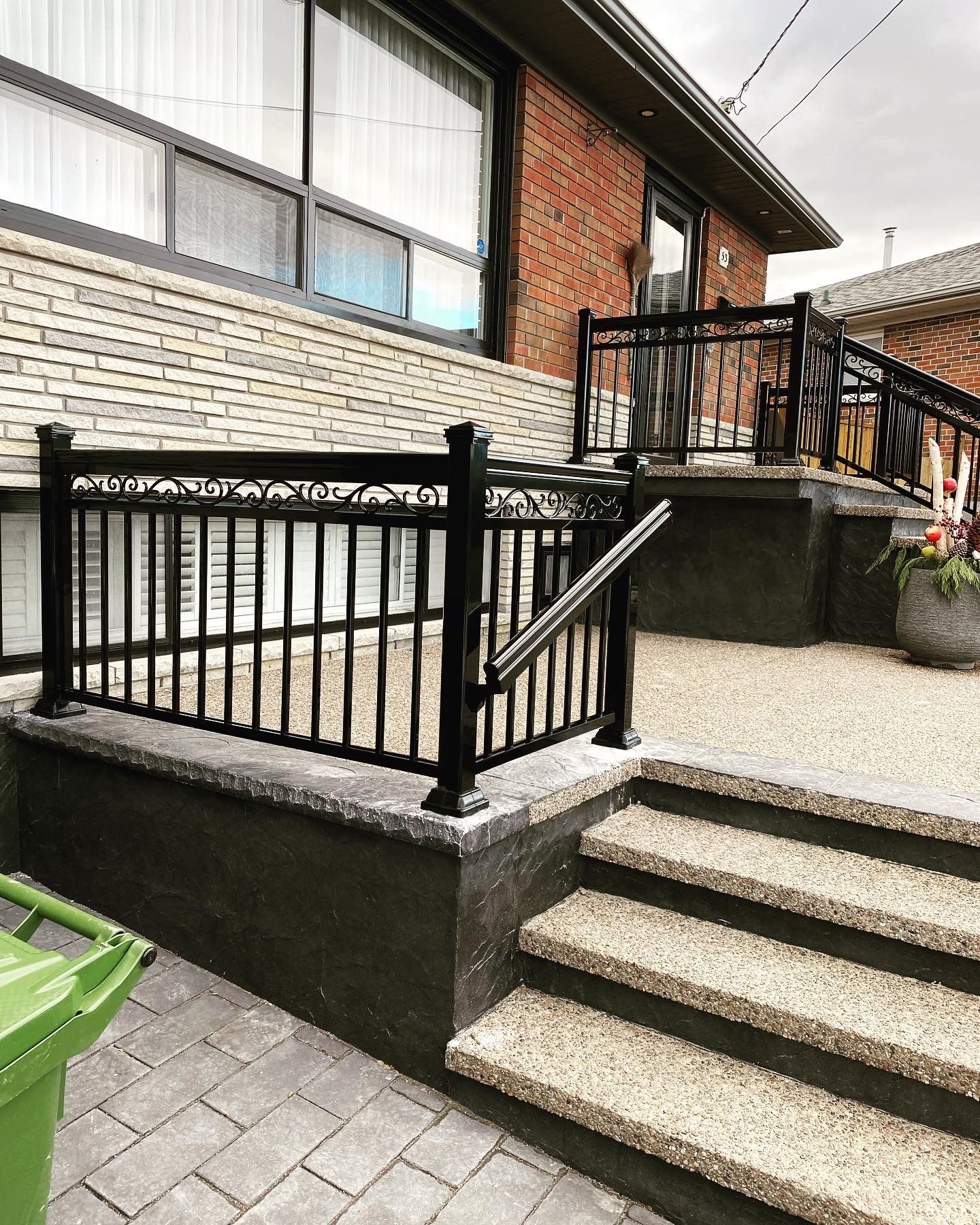 Black metal railing on a brick house's steps and a low wall, gravel steps leading up.