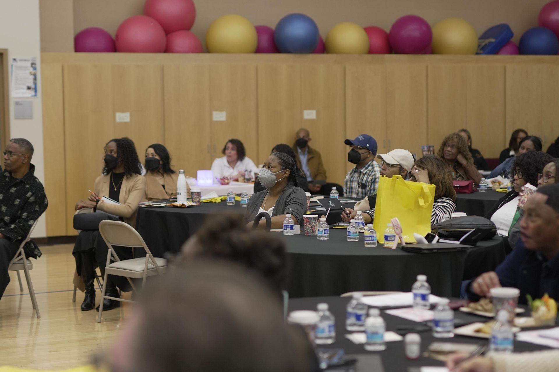 A group of people are sitting at tables in a gym.
