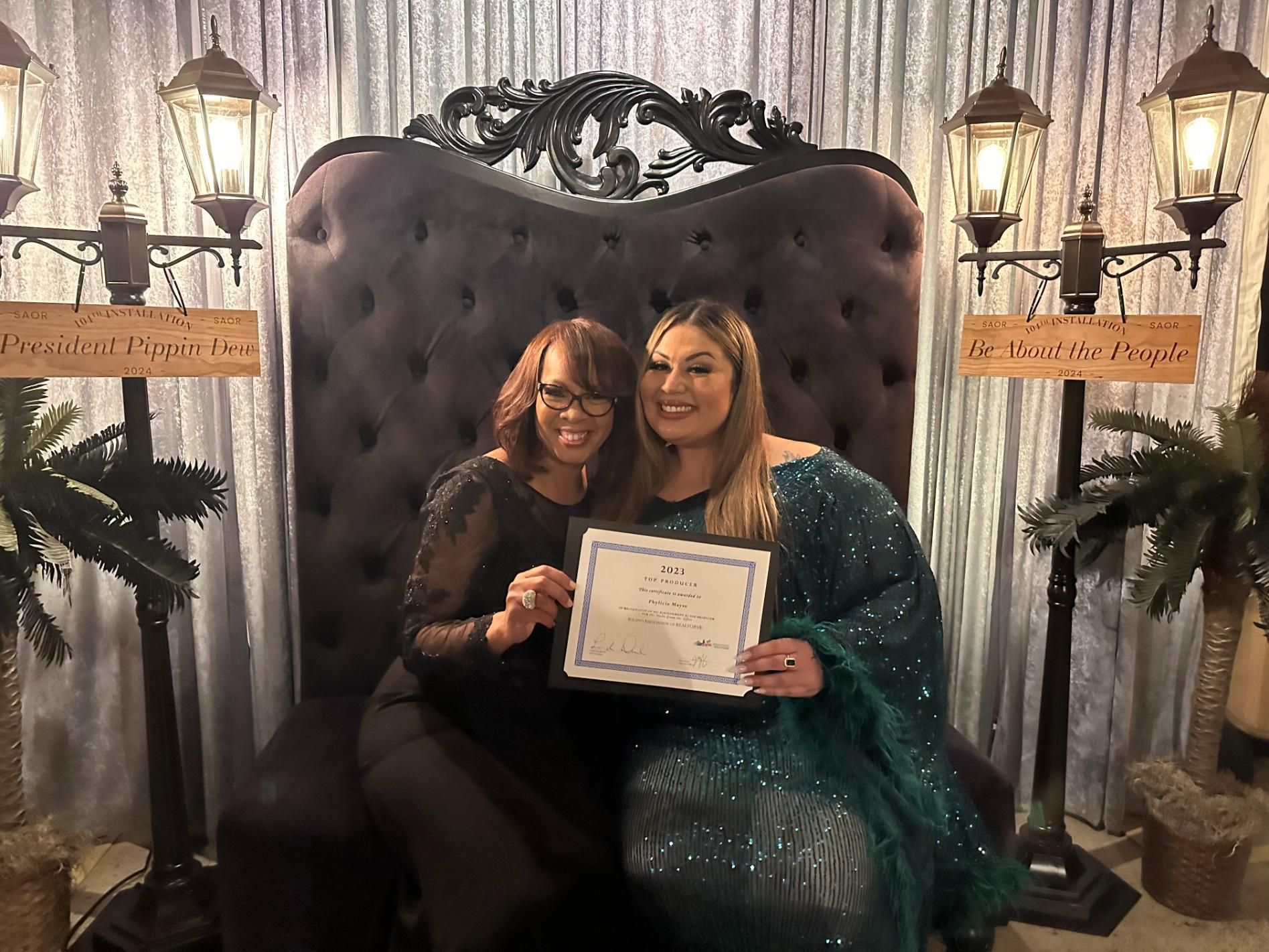 Two women are sitting in a chair holding a certificate.