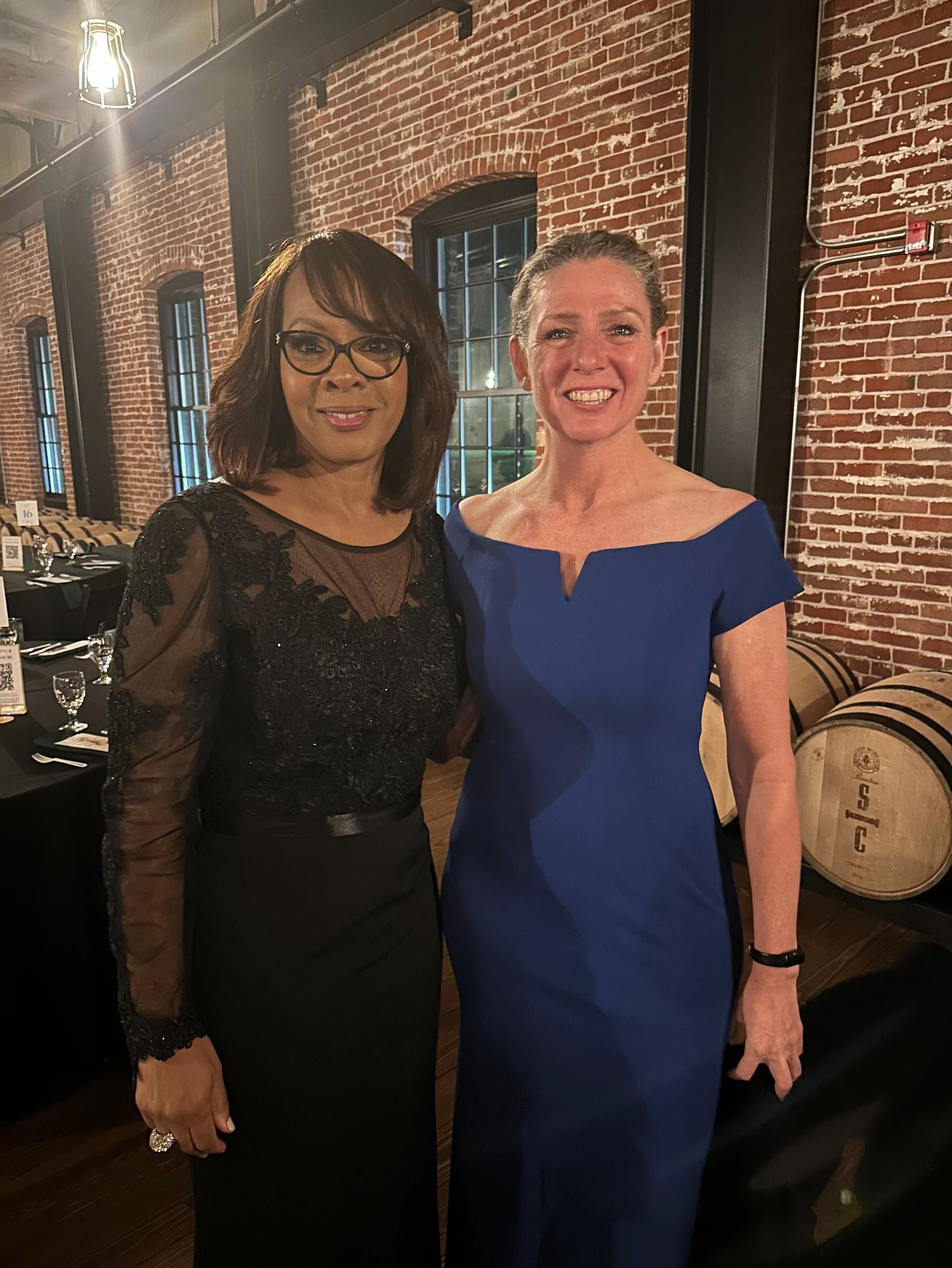 Two women are posing for a picture in front of a brick wall.