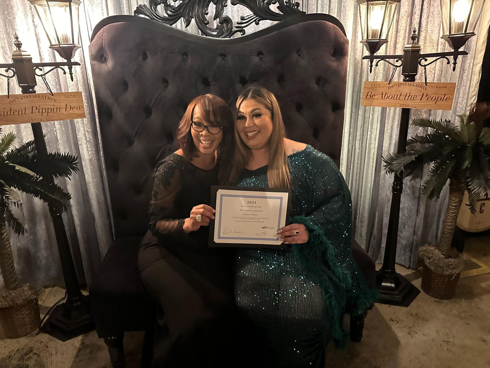 Two women are sitting in a chair holding a certificate.