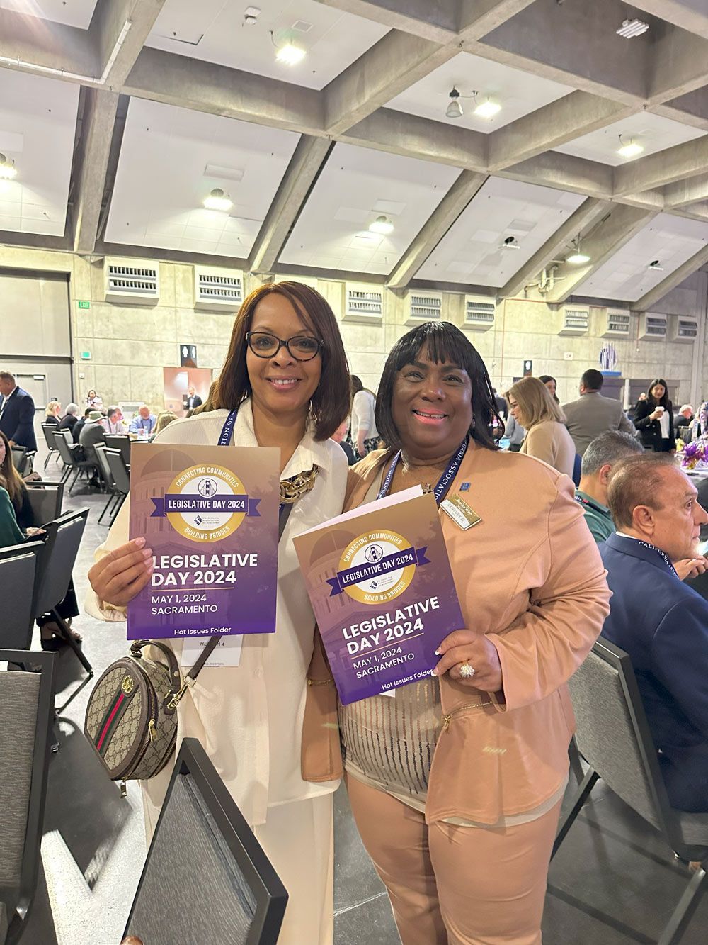 Two women are standing next to each other holding a book.