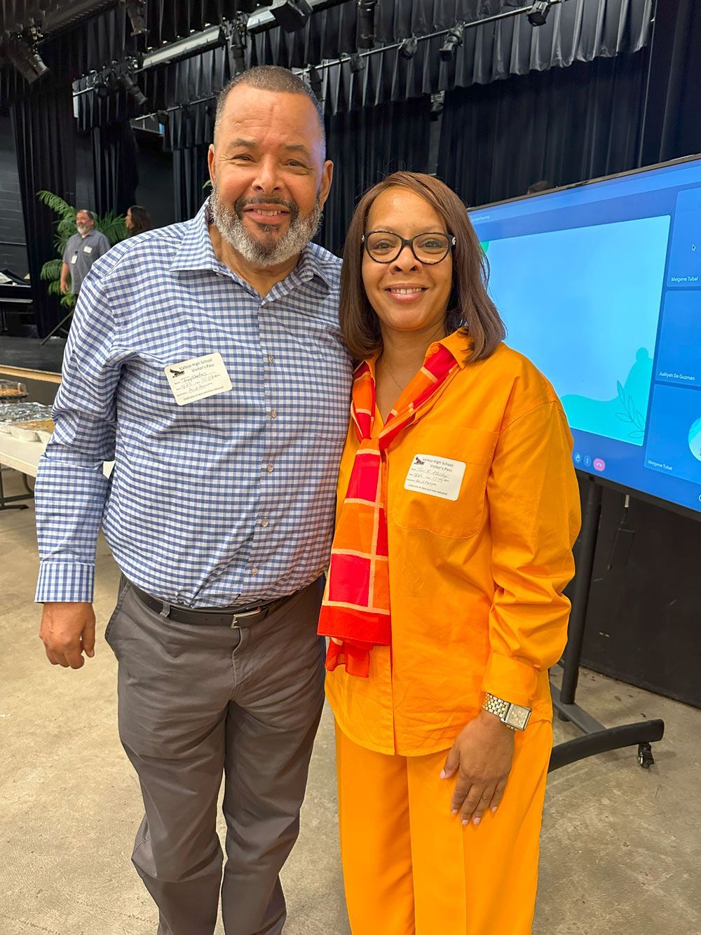 A man and a woman are posing for a picture in front of a screen.