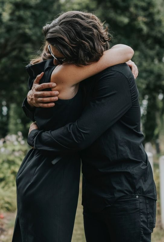 Two people in black clothing embrace outdoors.