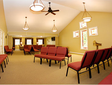 An empty chapel interior with red seating, beige walls and carpet, and arched ceiling.