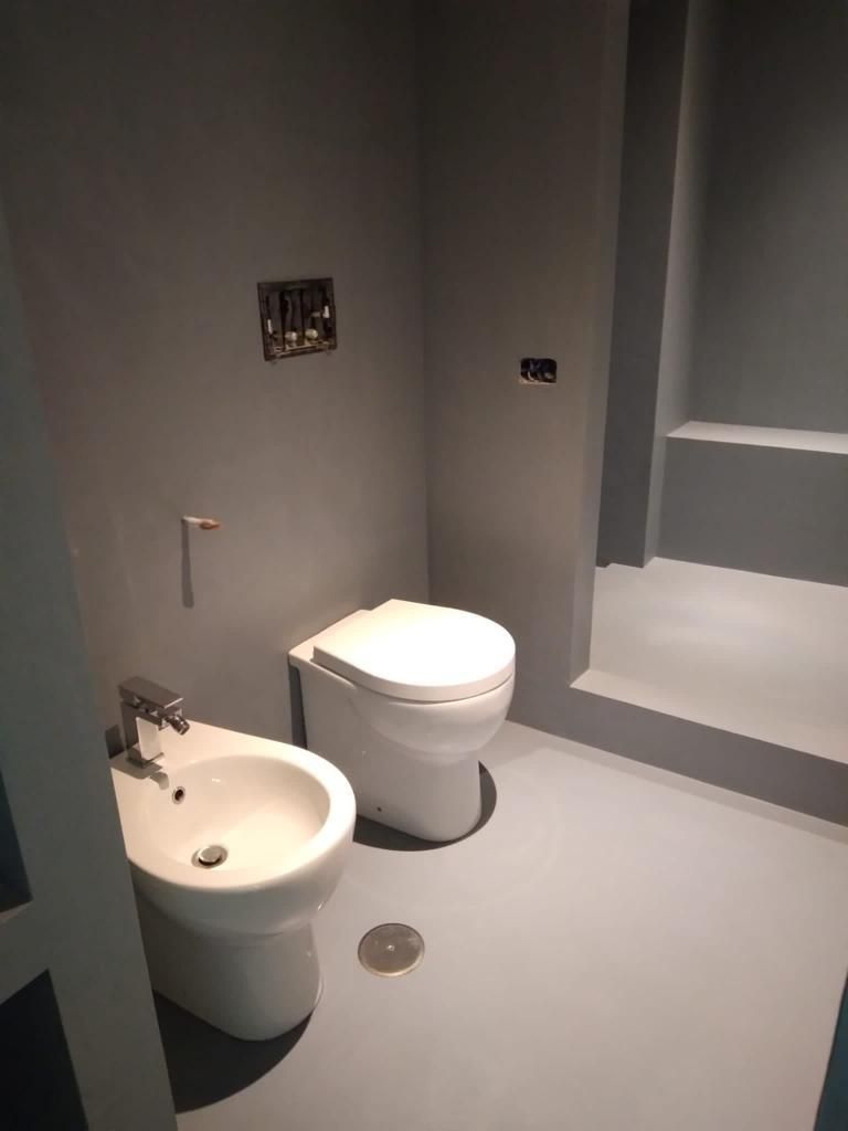 Un bagno moderno con bidet e WC bianchi su pareti e pavimento grigi.