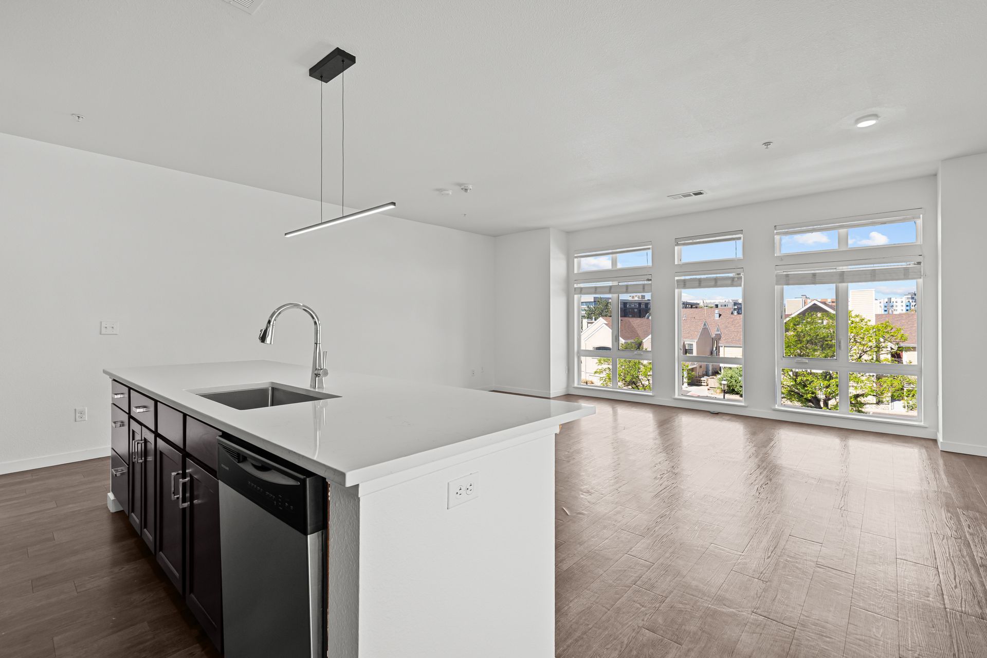 An empty kitchen with a sink , dishwasher , and large windows.