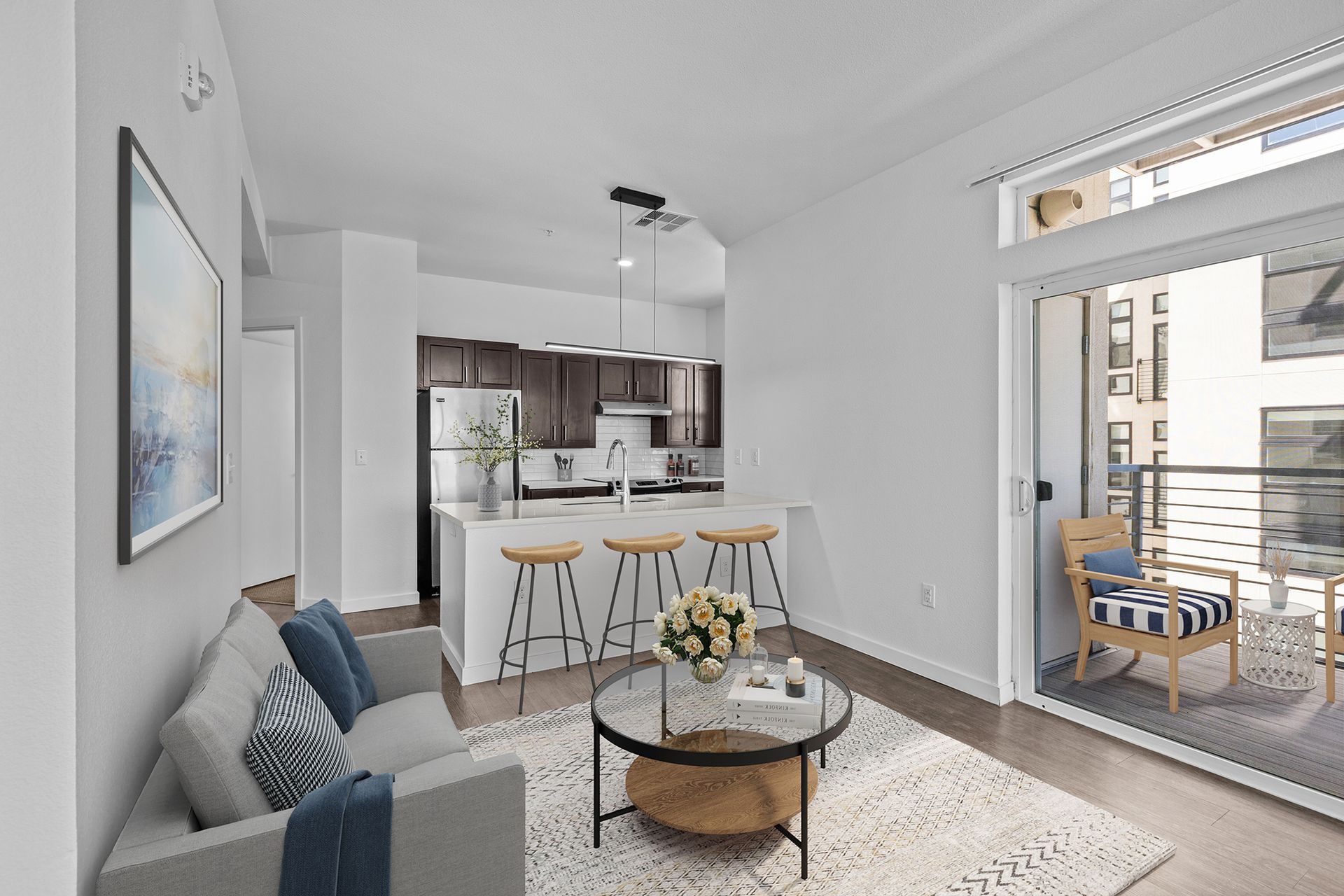A living room with a couch , table , chairs and sliding glass doors leading to a kitchen.