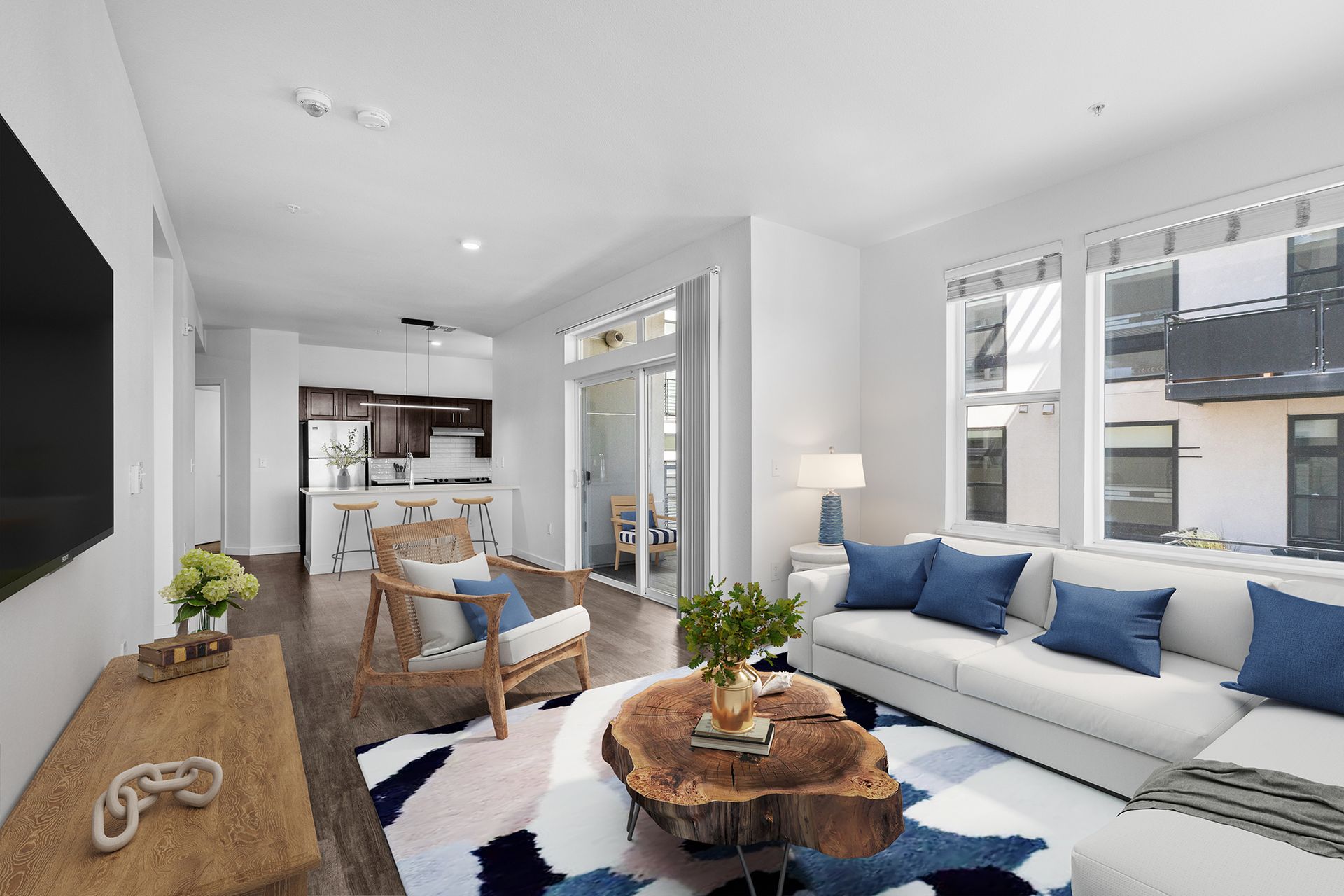 A living room with a white couch , blue pillows , a wooden table and a flat screen tv.