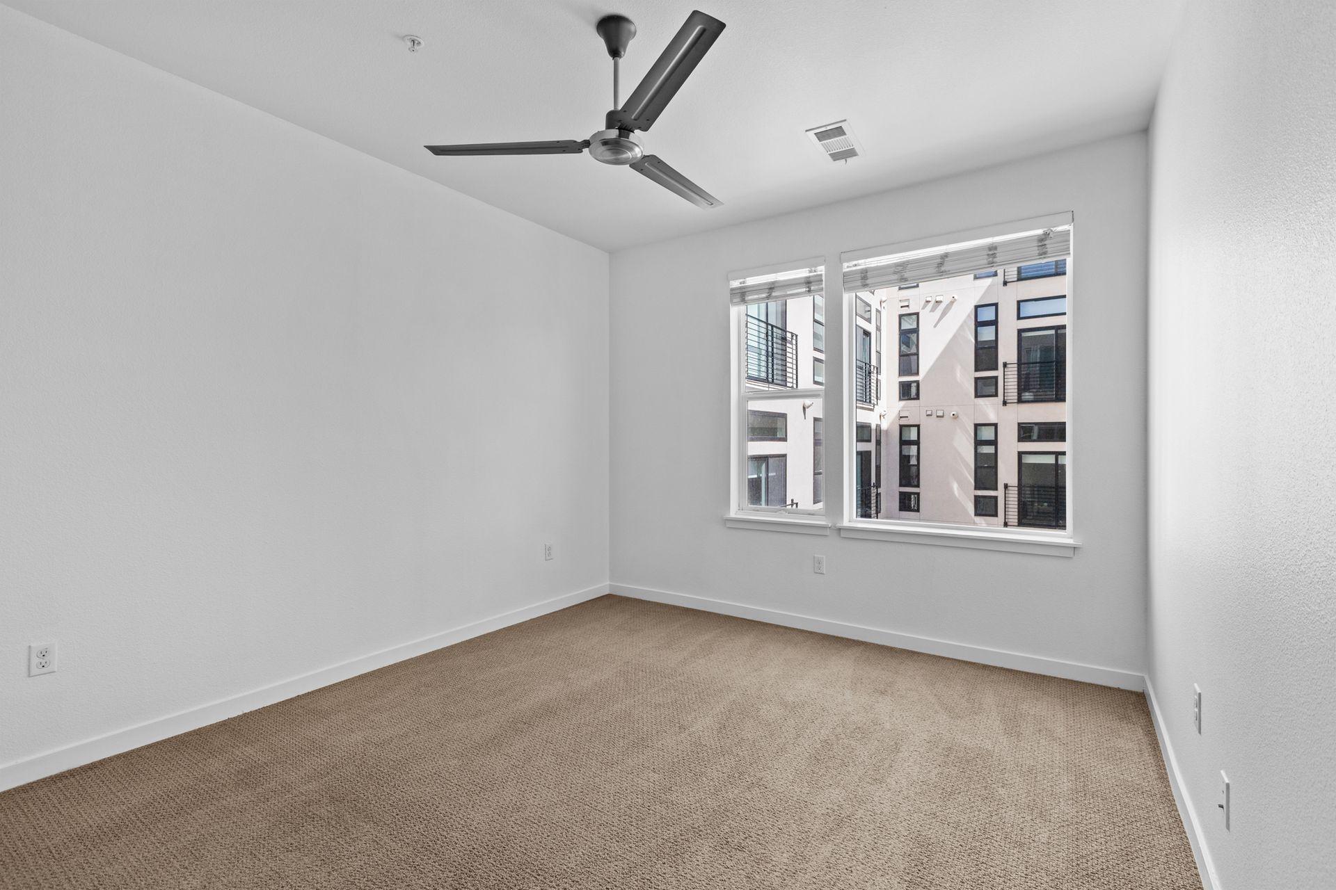An empty bedroom with a ceiling fan and two windows.