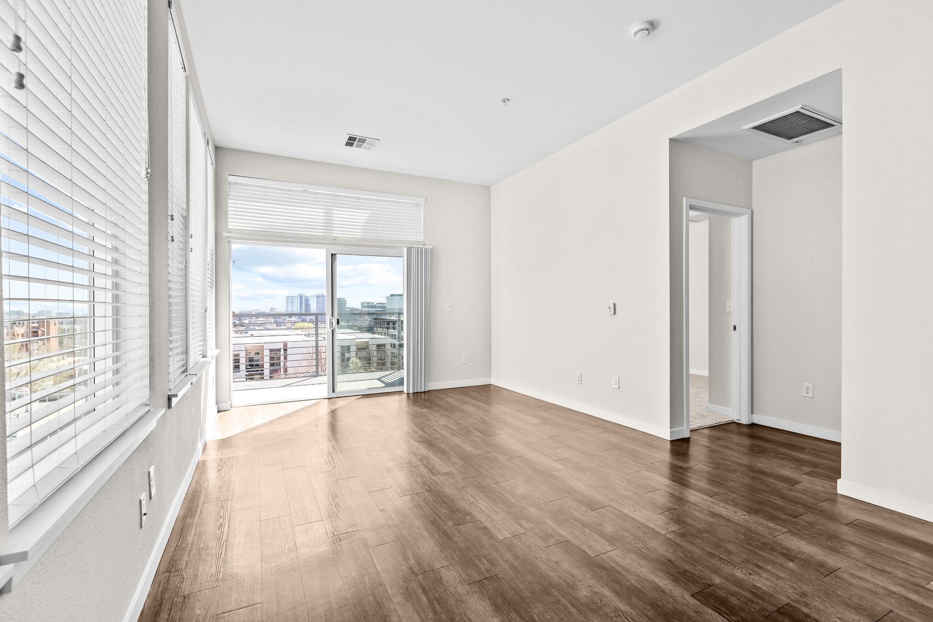 An empty living room with hardwood floors and a balcony.