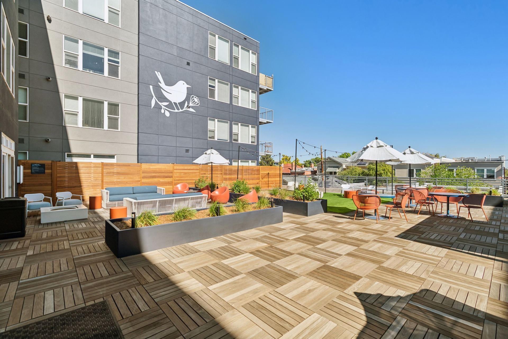 Outdoor patio with seating, umbrellas, and a large mural of a bird.