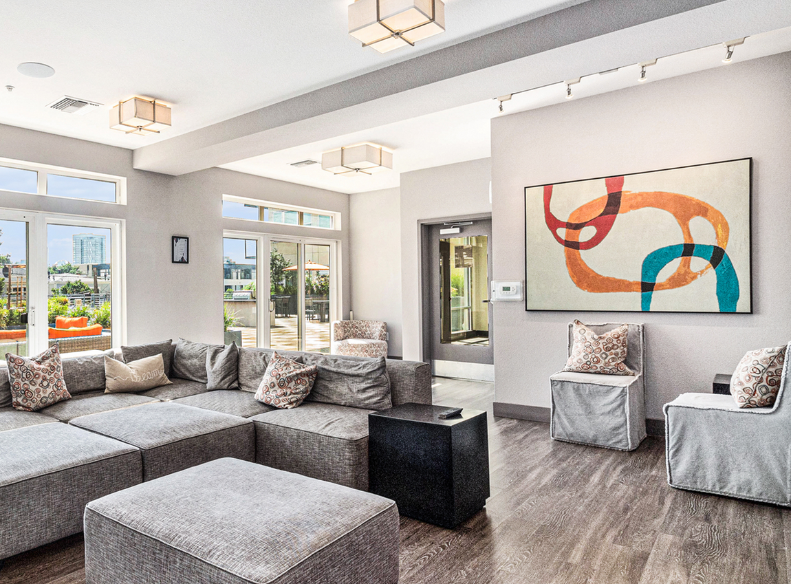 A clubhouse with a couch , chairs , ottomans and a large painting on the wall.