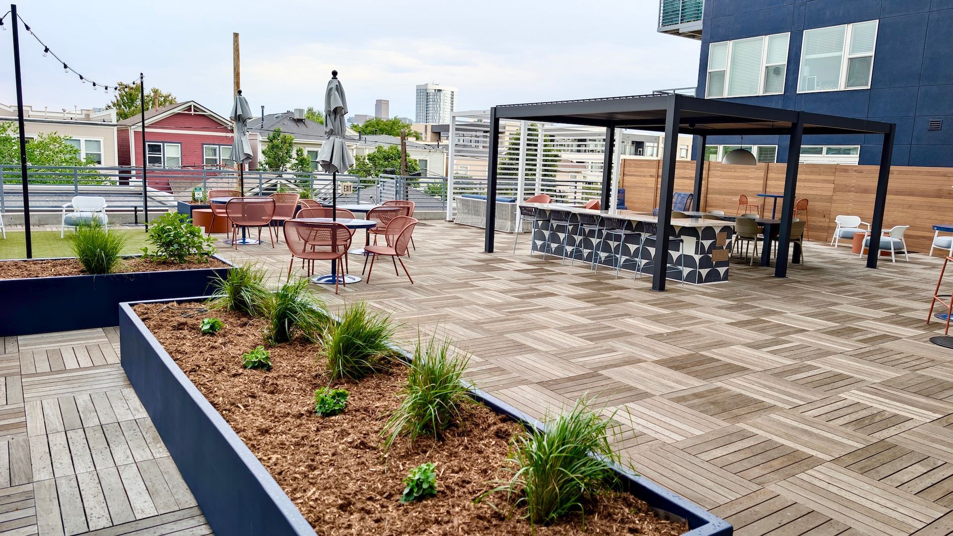 Rooftop patio with bar, tables, and planters; brick and wooden building backdrop, overcast sky.