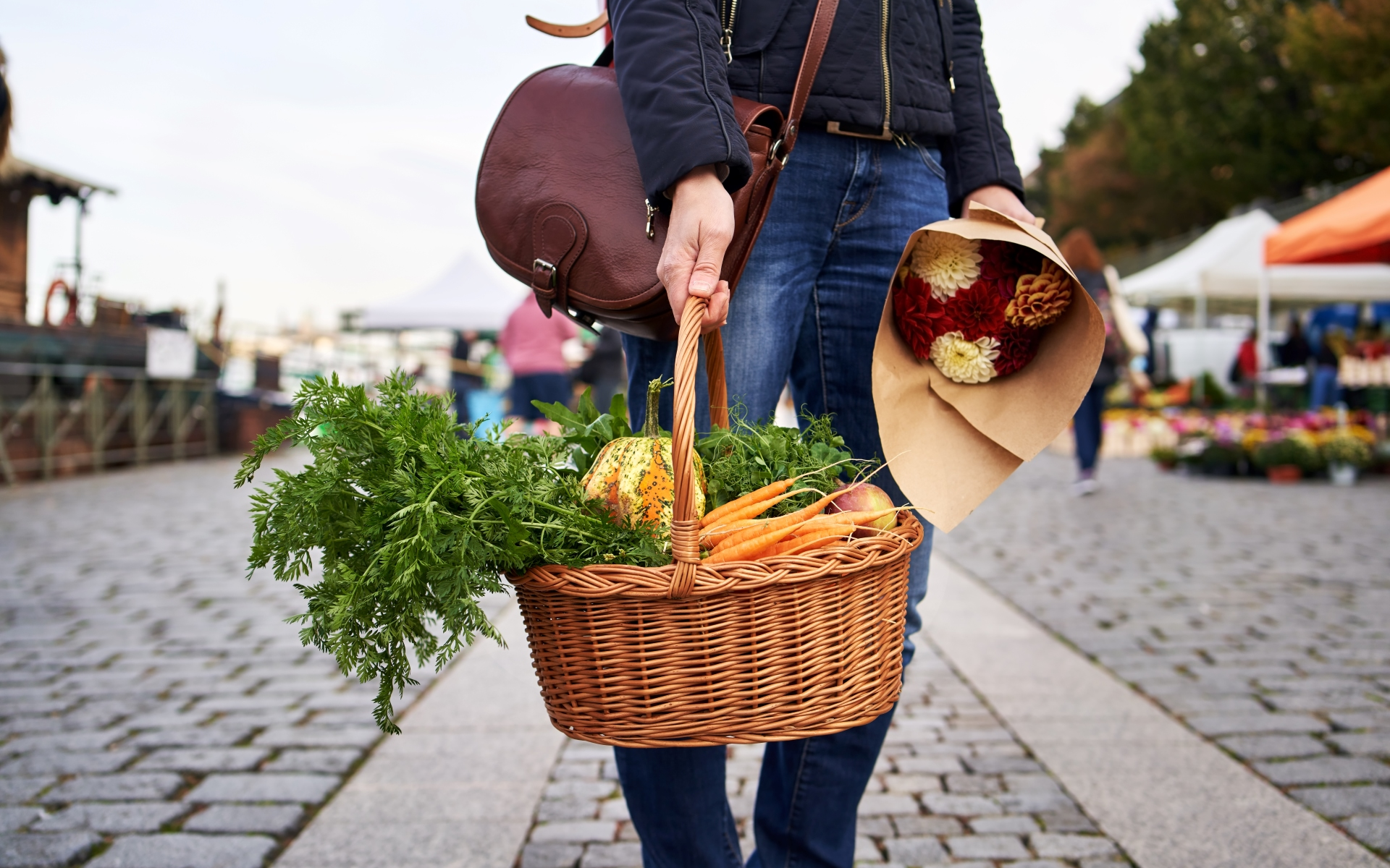 A woman is carrying a basket of vegetables and a bouquet of flowers.