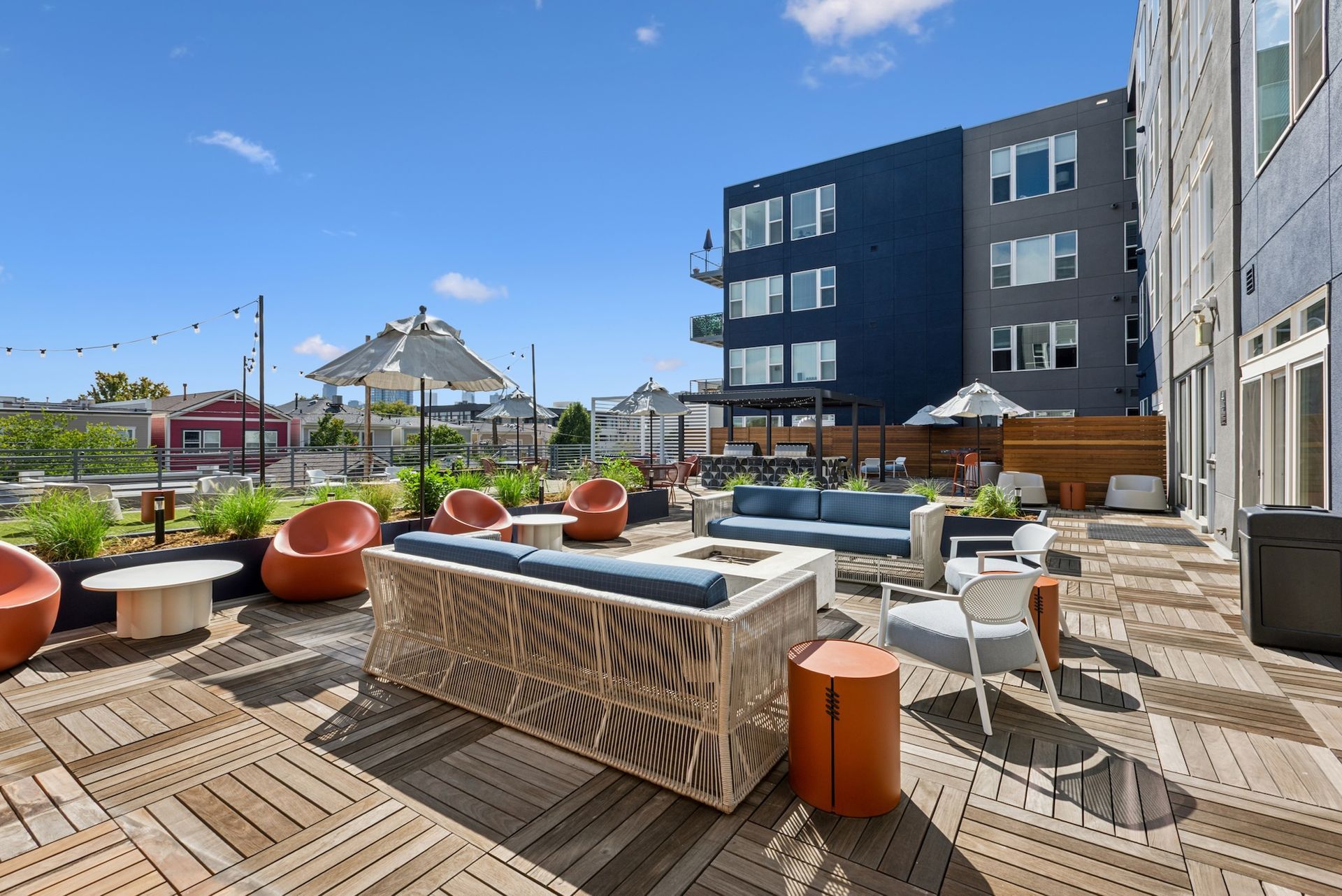 Rooftop patio with seating areas, fire pit, and blue building on a sunny day.