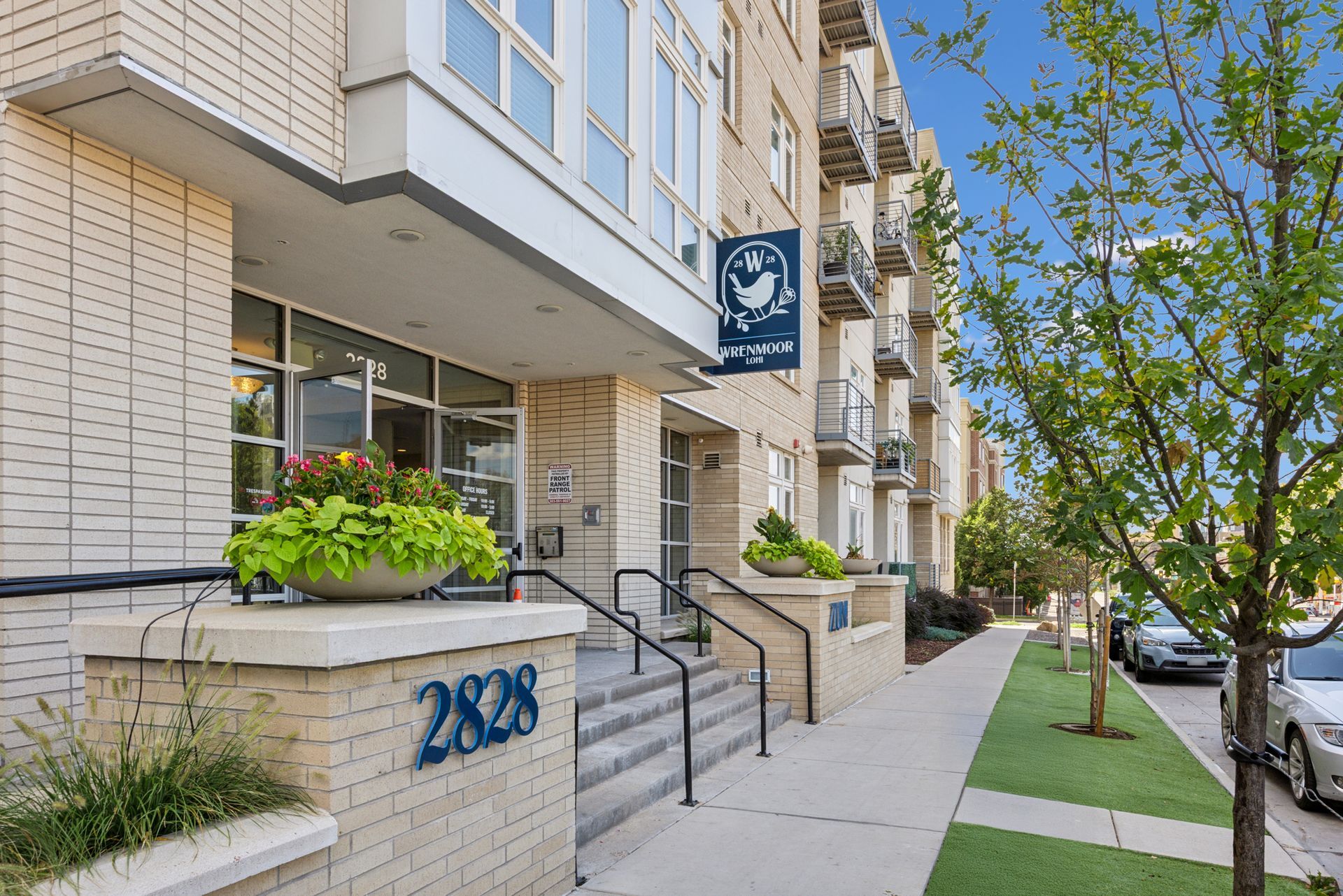 Apartment building entrance with address 2828, sidewalk, and parked cars.