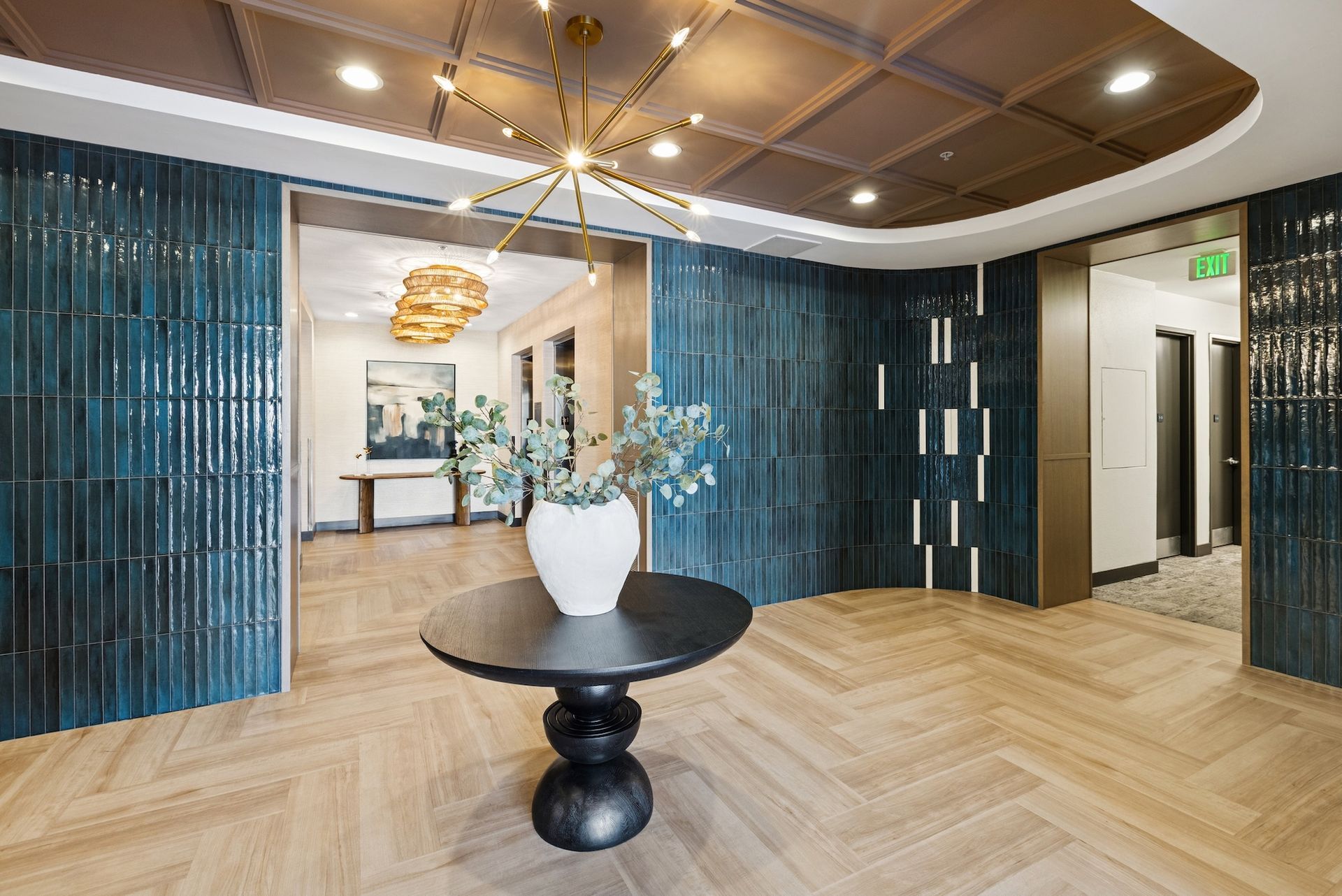 Stylish lobby with herringbone floors, teal tile walls, round table, and a starburst chandelier.