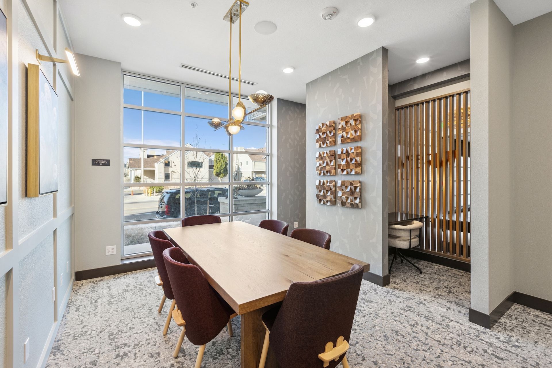 Conference room with a wooden table, burgundy chairs, and a large window overlooking a street.