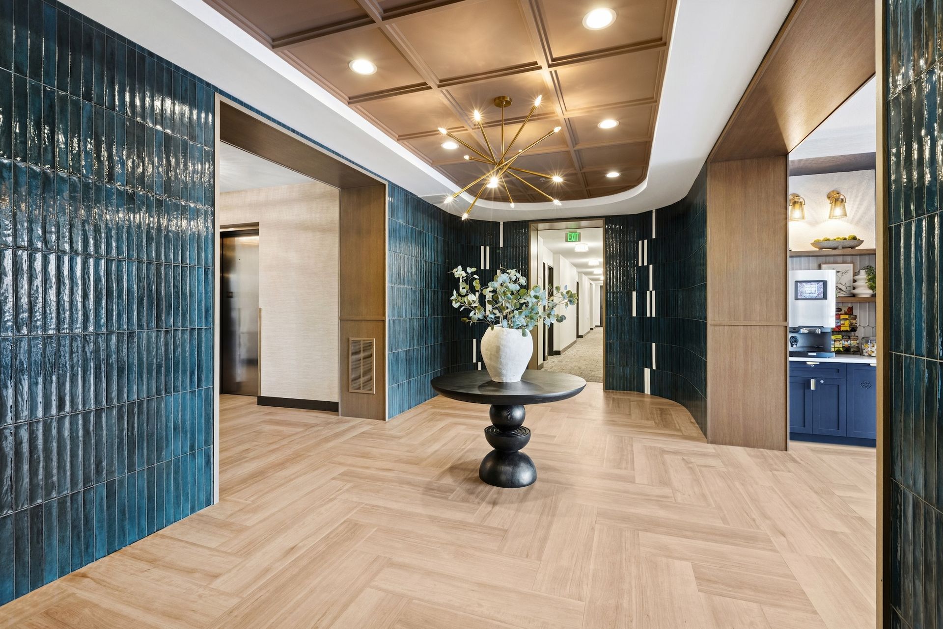 Stylish hallway with teal tile walls, wood floor, and a round table with a vase of flowers.