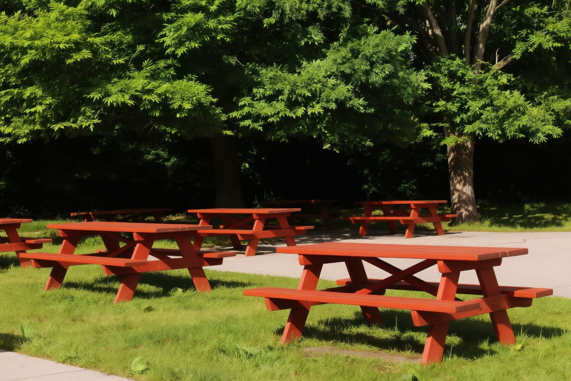Empty red picnic tables sit on rich green grass under large trees in park. Empty red picnic tables sit on rich green grass under large trees in park.