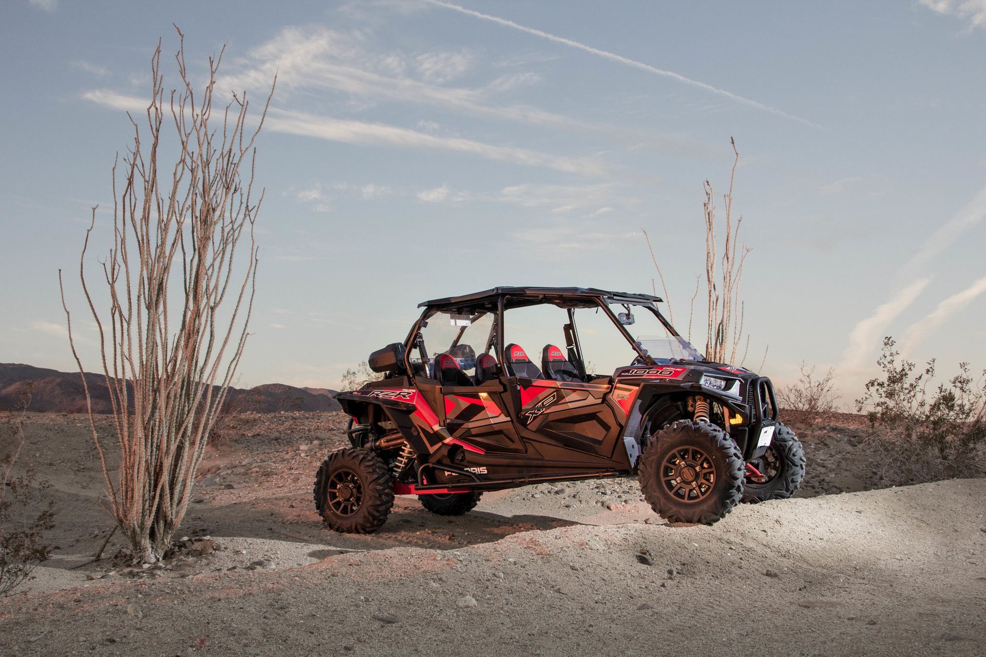 A red atv is parked on the side of a dirt road in the desert.