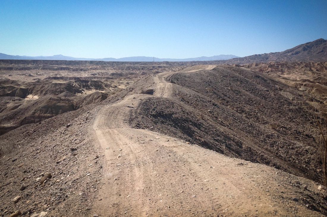 A dirt road in the desert with mountains in the background.