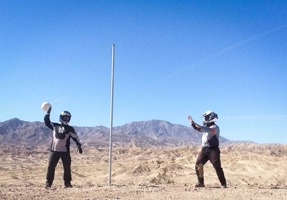 Two people playing volleyball in the desert with mountains in the background
