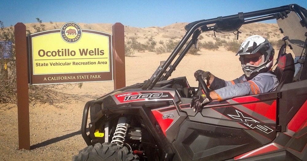 A man is riding a atv in the desert in front of a sign that says ocotillo wells.