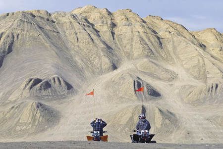 Two people are riding atvs in front of a mountain.