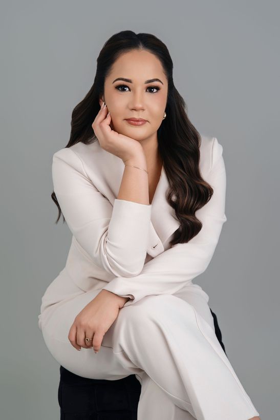 A woman is sitting at a desk with a laptop and a vase of flowers.