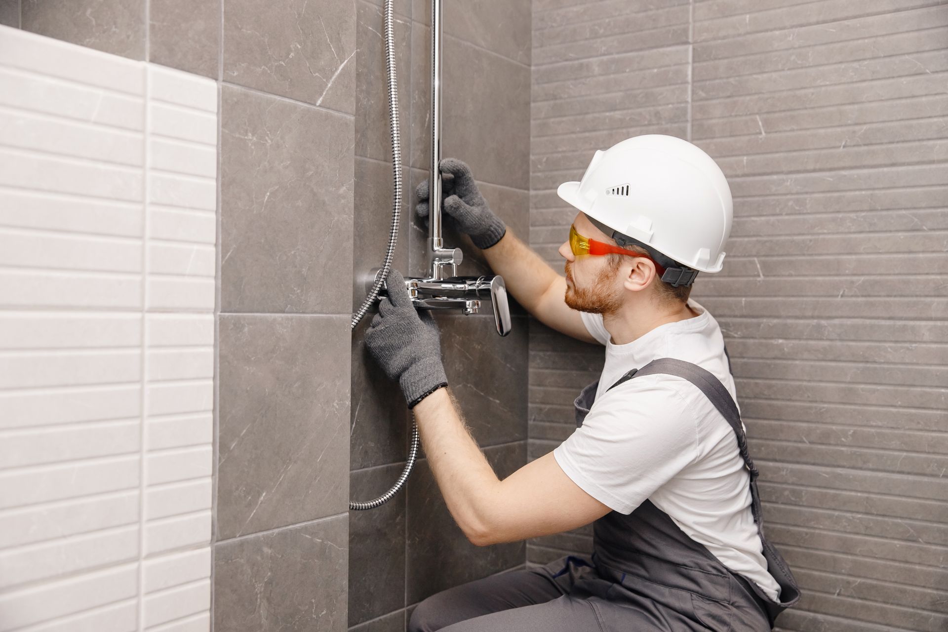 A plumber is installing shower fixtures in a bathroom.
