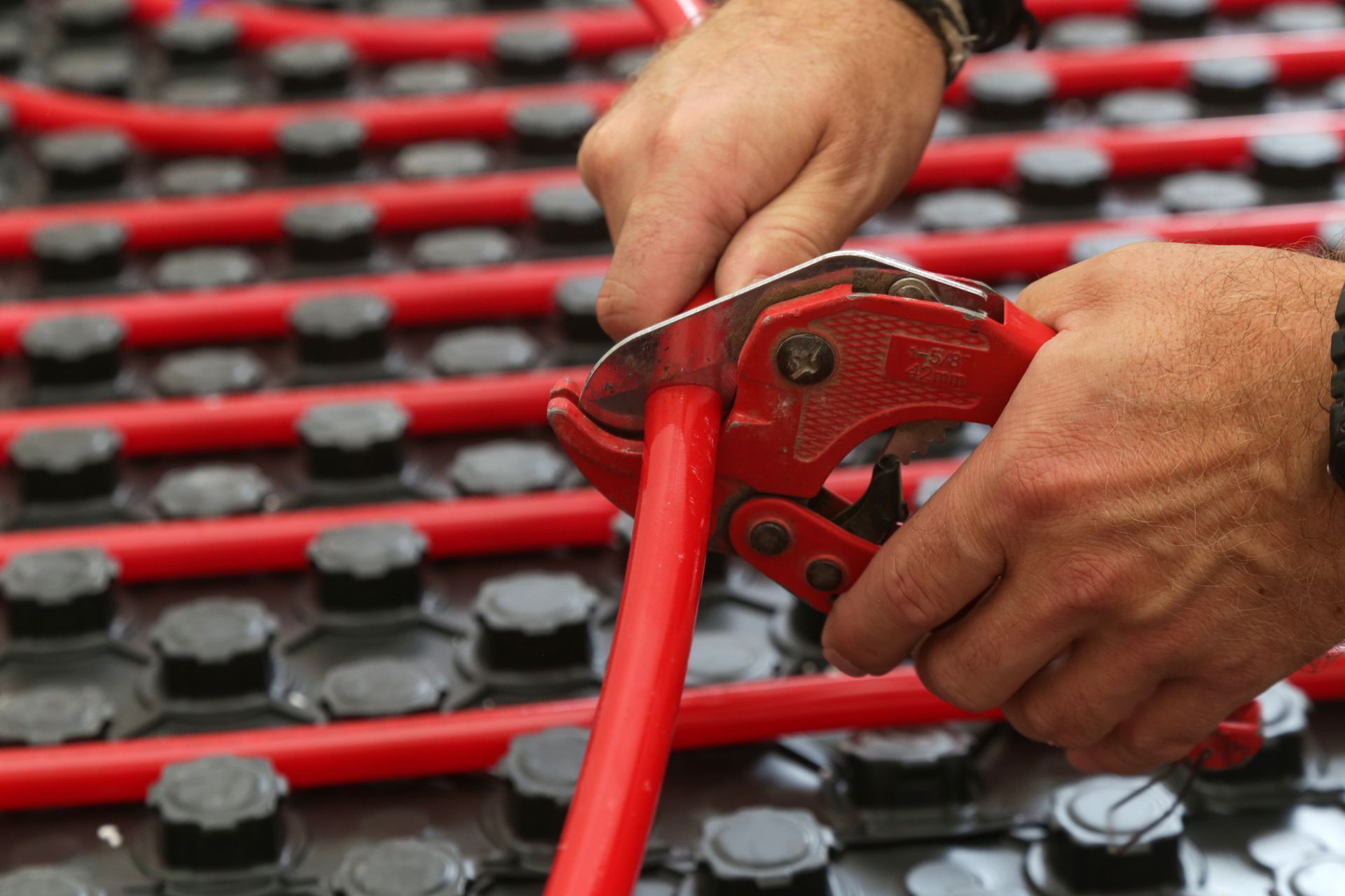 A person is cutting a red pipe with a pair of pliers.