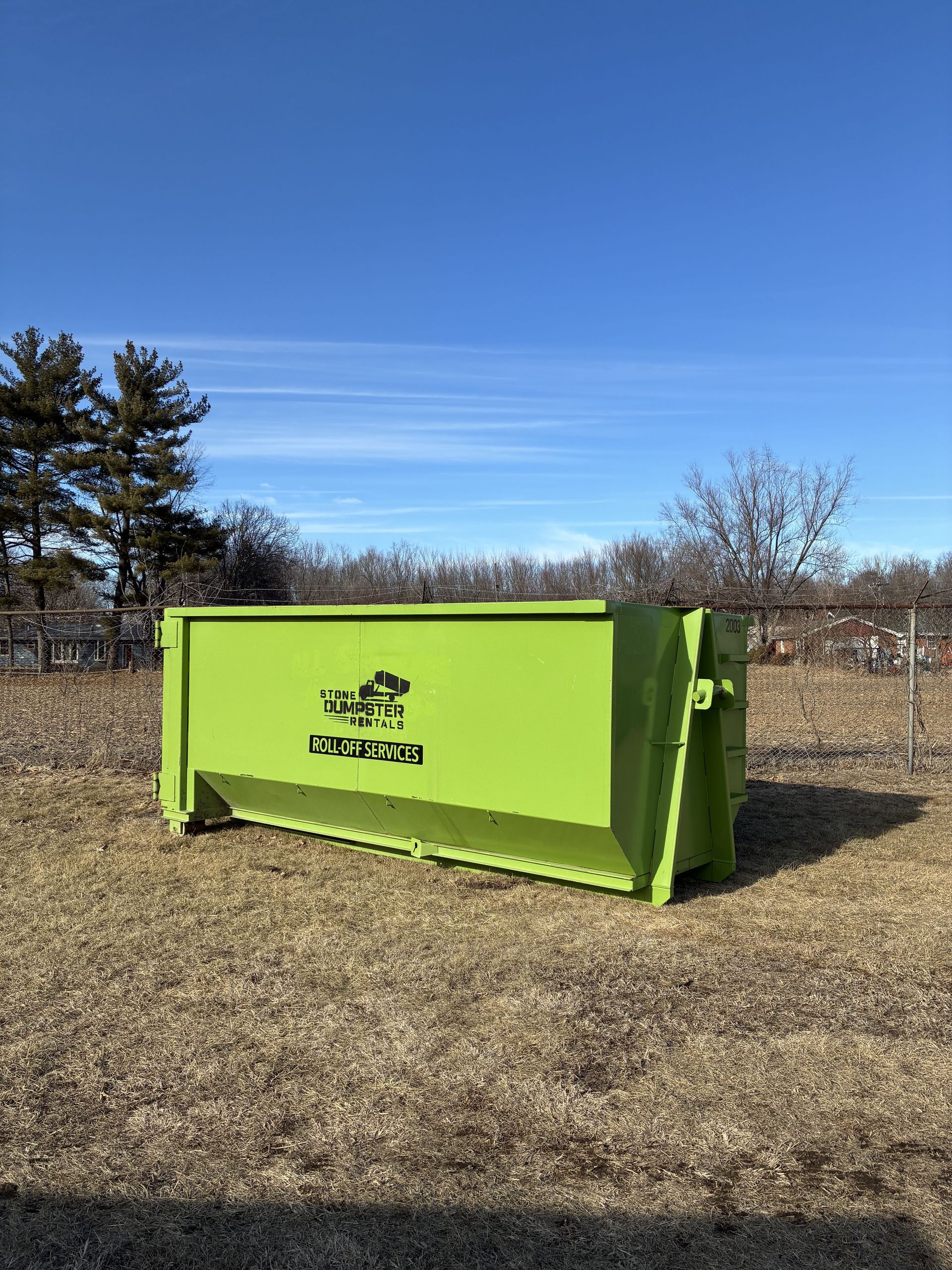 A large, black rectangular metal dumpster sits on a concrete driveway in front of a residential garage.