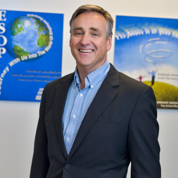 A man in a suit stands in front of a poster that says journey with us into the world