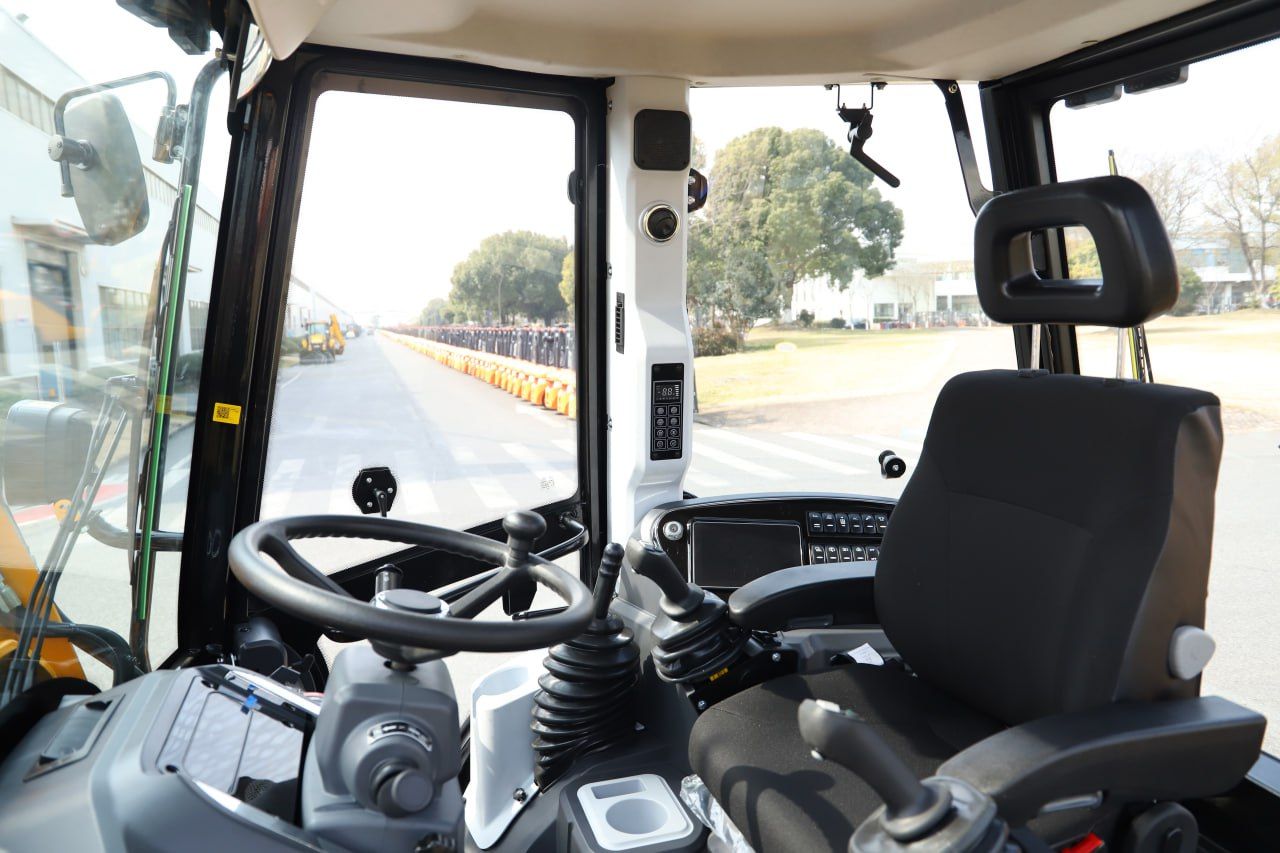 Interior of heavy machinery cab with steering wheel, seat, and view of outdoor setting.