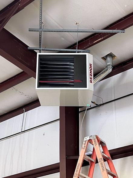 A Reznor industrial heater suspended from the ceiling of a building above an orange ladder.