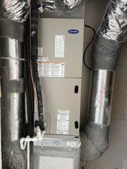 Carrier HVAC air handler unit installed in a utility closet with insulated silver ductwork attached to the sides.
