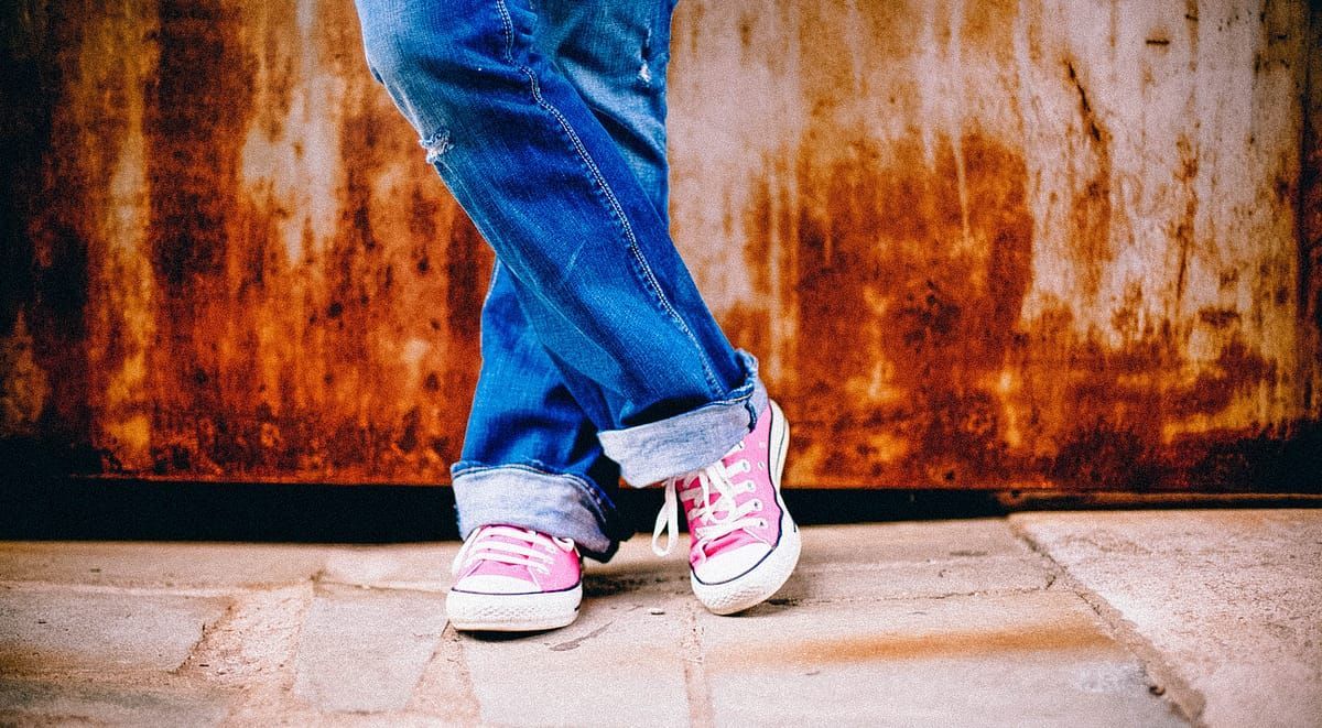 a person wearing pink sneakers and blue jeans is standing on a sidewalk .