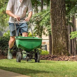 a man is spreading fertilizer on a lush green lawn with a wheelbarrow .