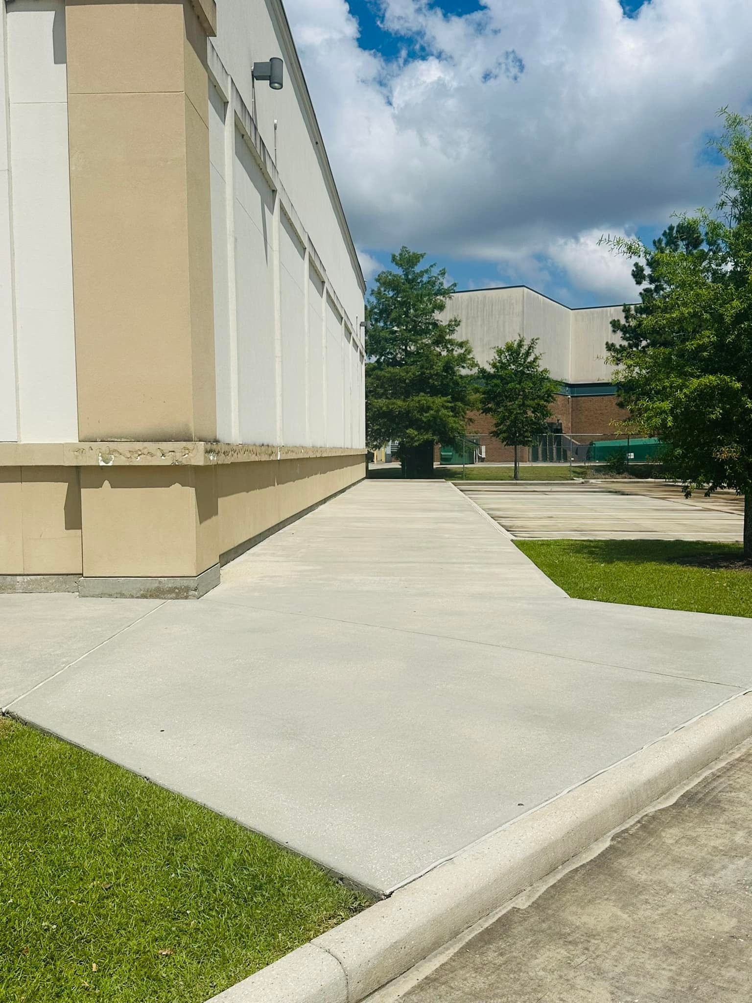 Concrete walkway next to a building, green grass, and trees under a cloudy sky.