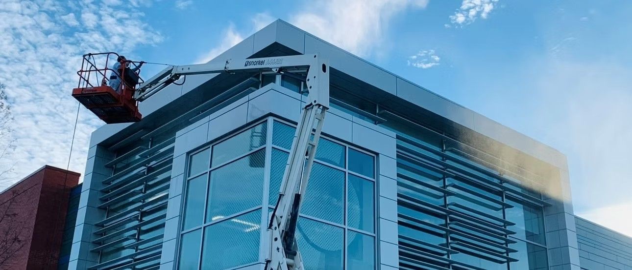 A cherry picker platform with a person working on the facade of a modern building under a blue sky.