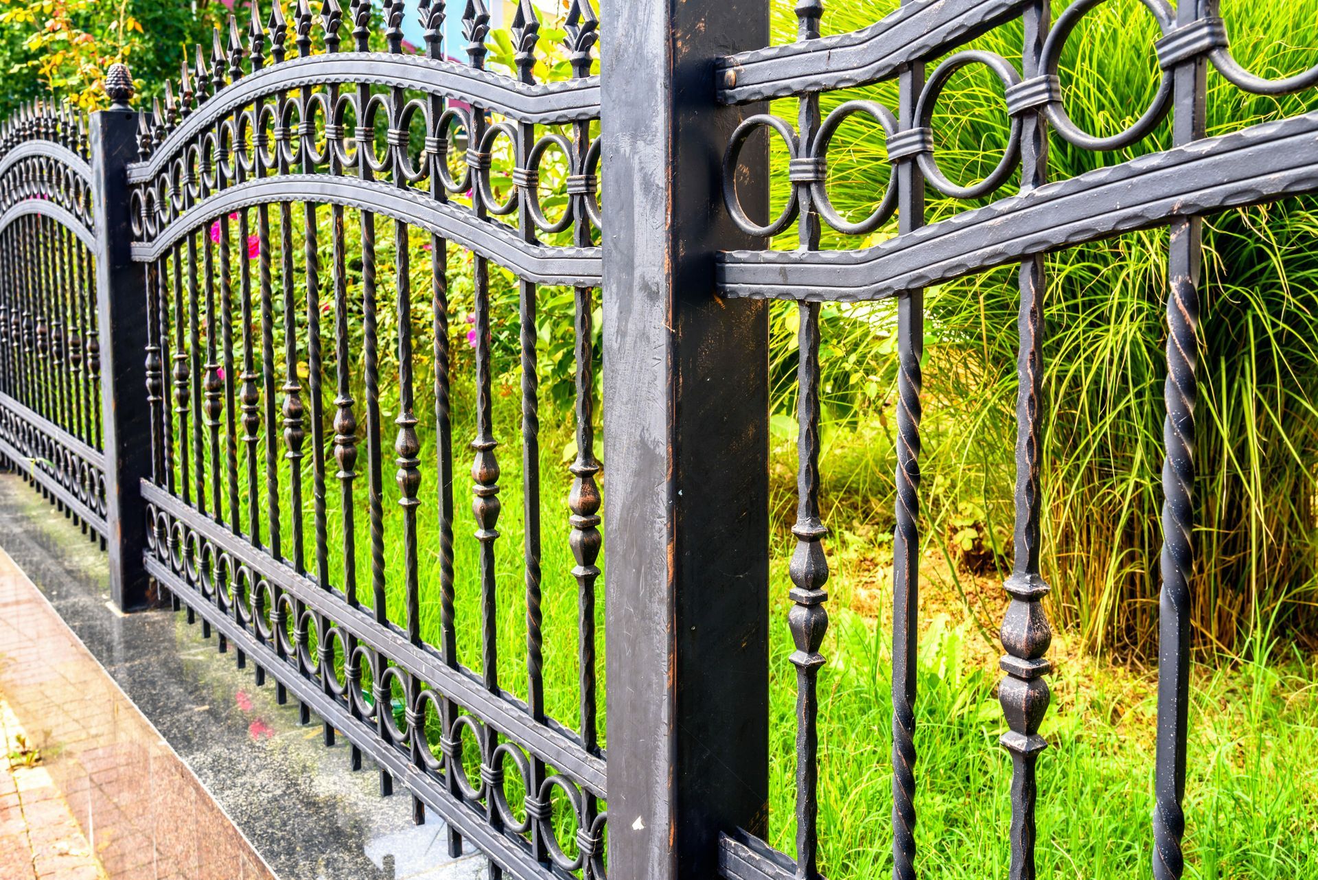 Decorative black iron fence with curved details lining a lush green garden walkway.
