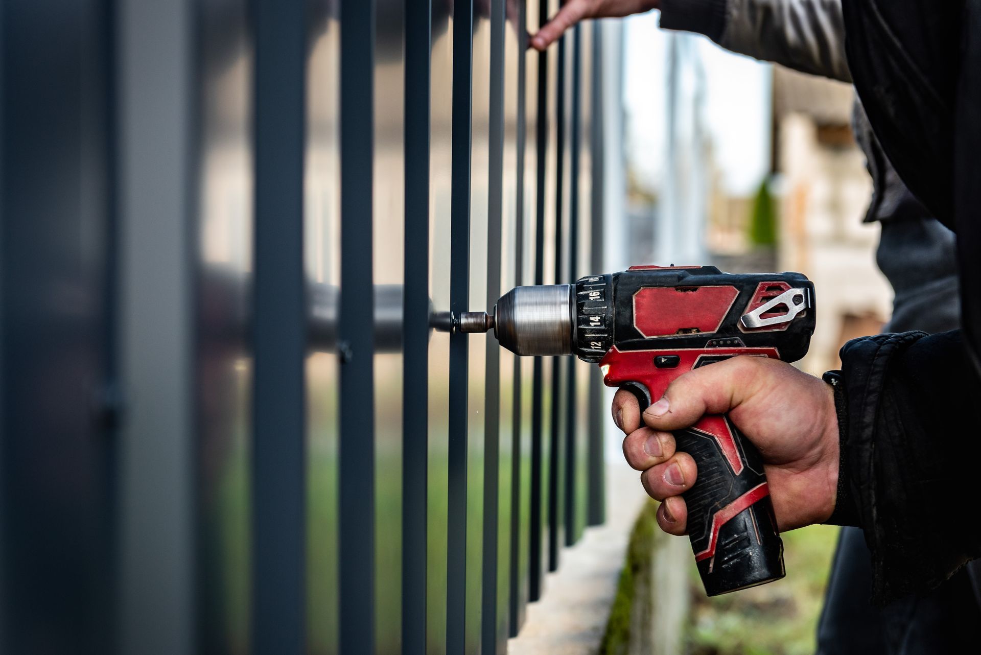 Hand holding a cordless drill fastening a screw into a metal fence railing. Hand holding a cordless drill fastening a screw into a metal fence railing.