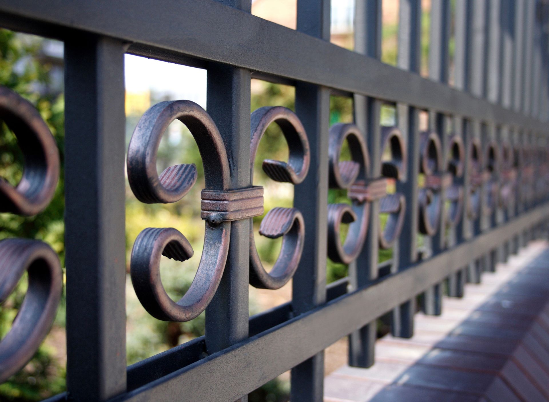 Close-up of black wrought iron fence with decorative scrollwork in sunlight. Close-up of black wrought iron fence with decorative scrollwork in sunlight.