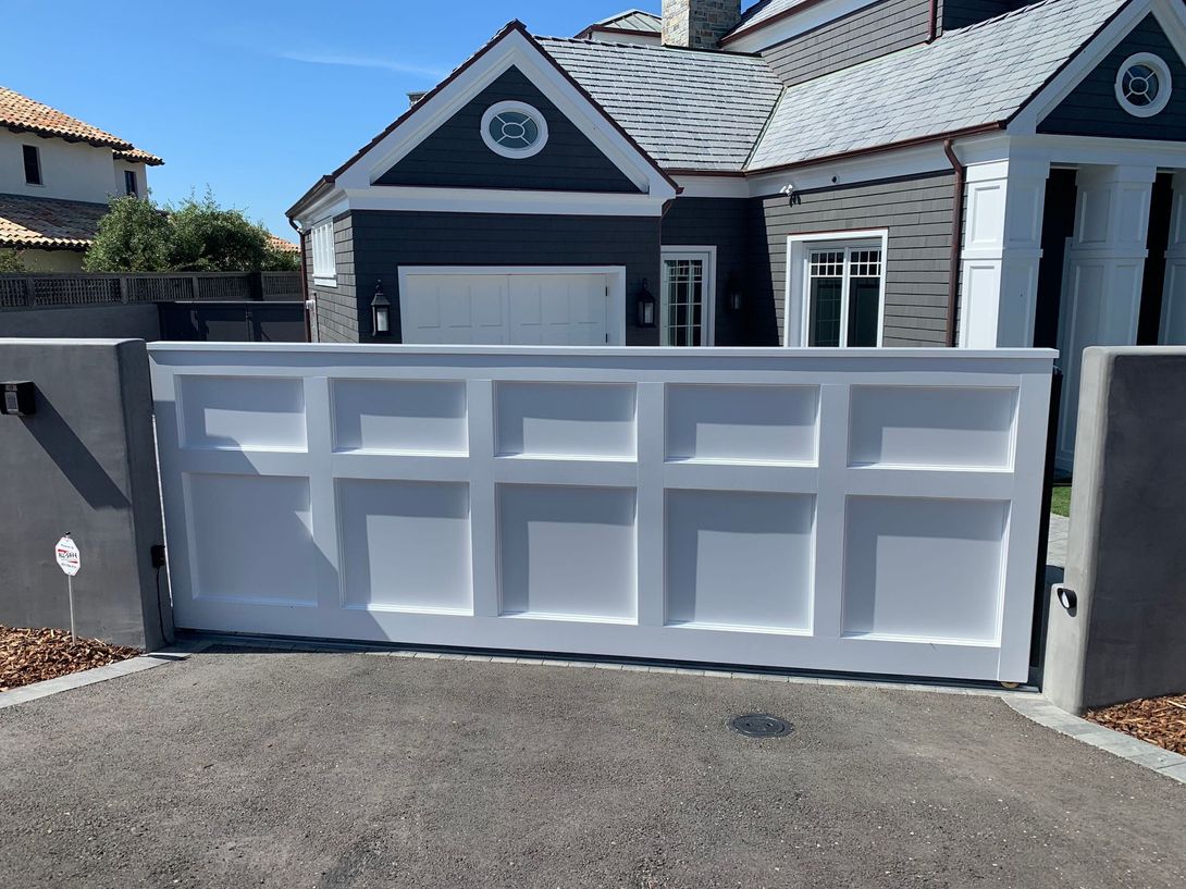 White paneled driveway gate in front of a modern home with gray siding.