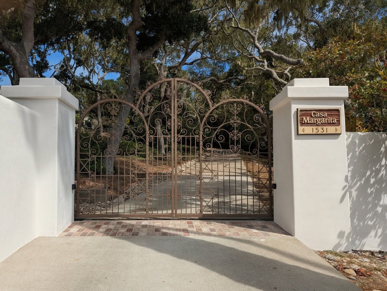 Iron gate with decorative arches, between white pillars with a sign. Entrance to 
